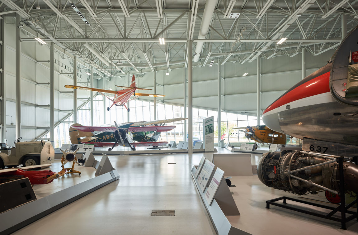 inside an aircraft museum, multiple planes are visible on the floor and suspended from the ceiling
