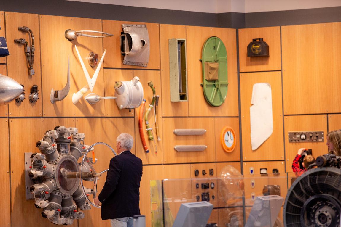 an elderly gentleman stands in front of an interactive wall of airplane components