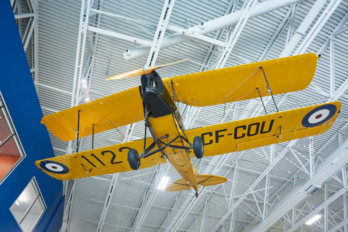 a yellow bi-plane suspended overhead in a museum
