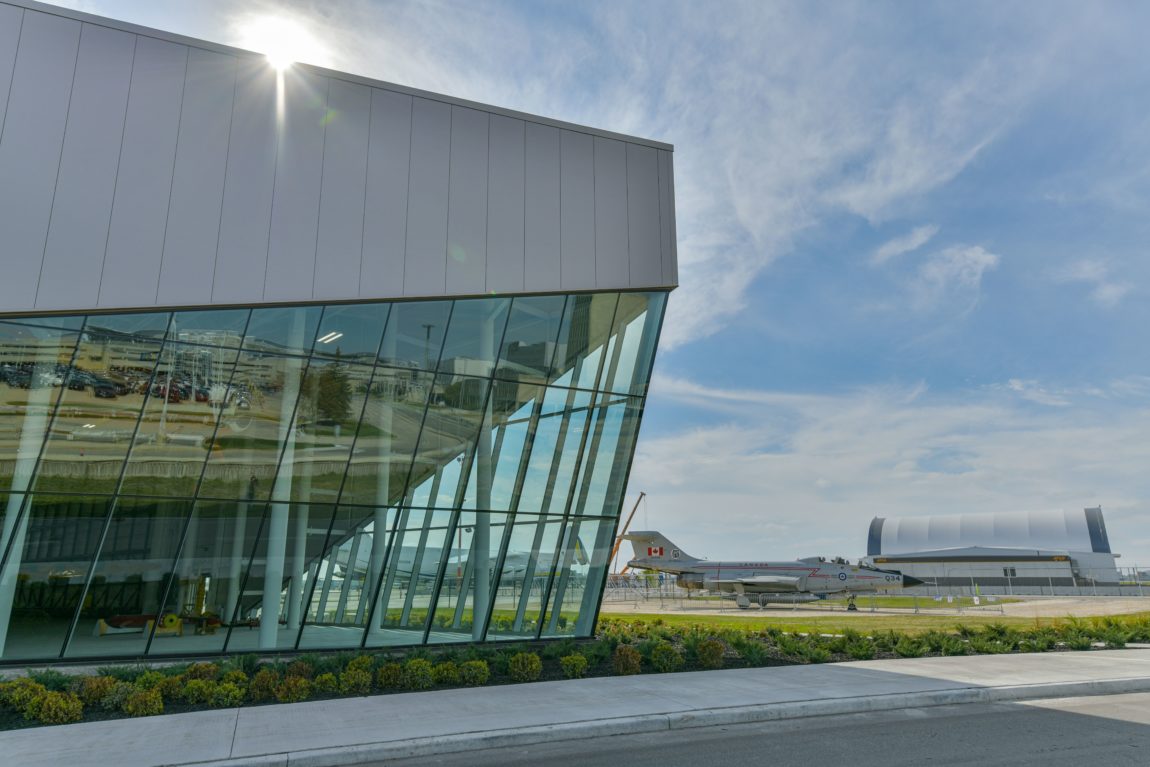a vintage fighter jet sits outside a large glass and metal building