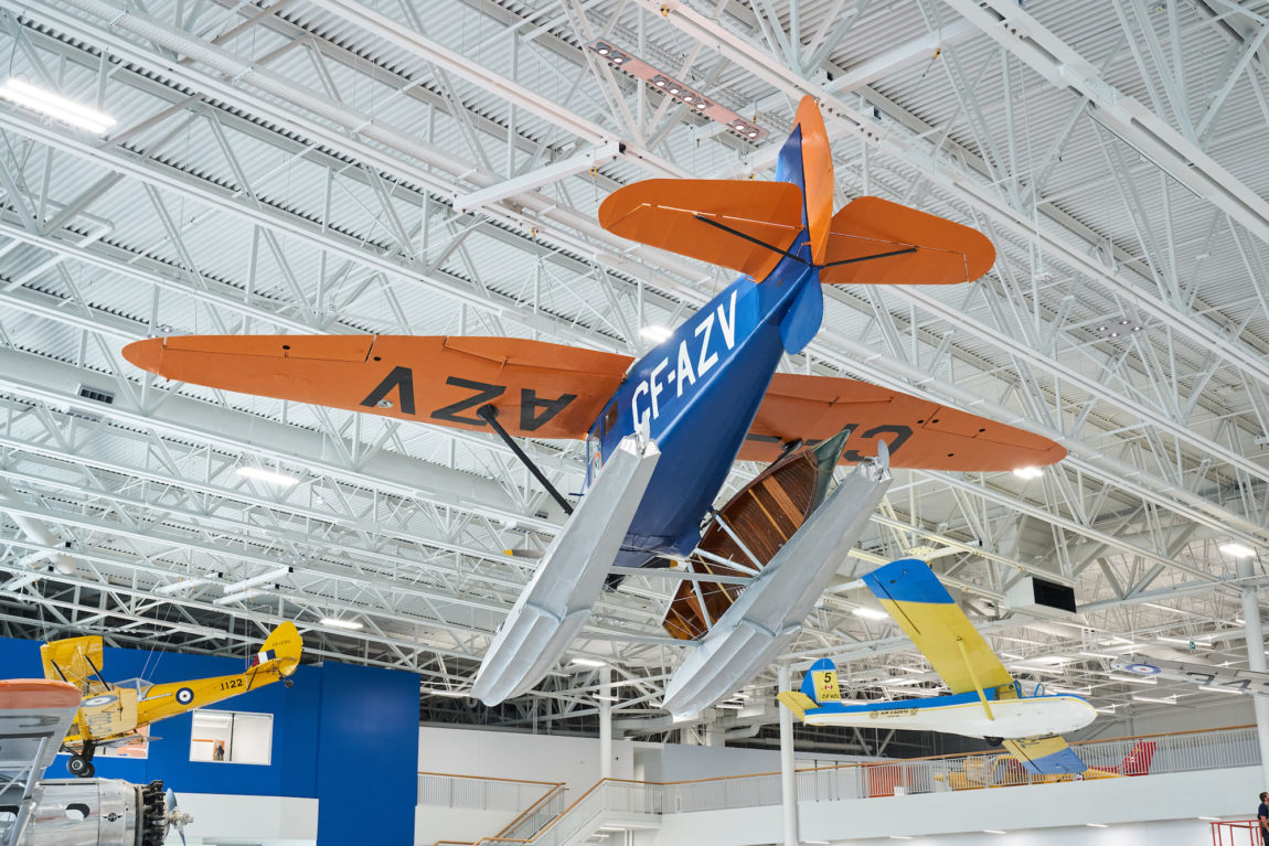 a vintage bushplane hangs suspended overhead in an aviation museum