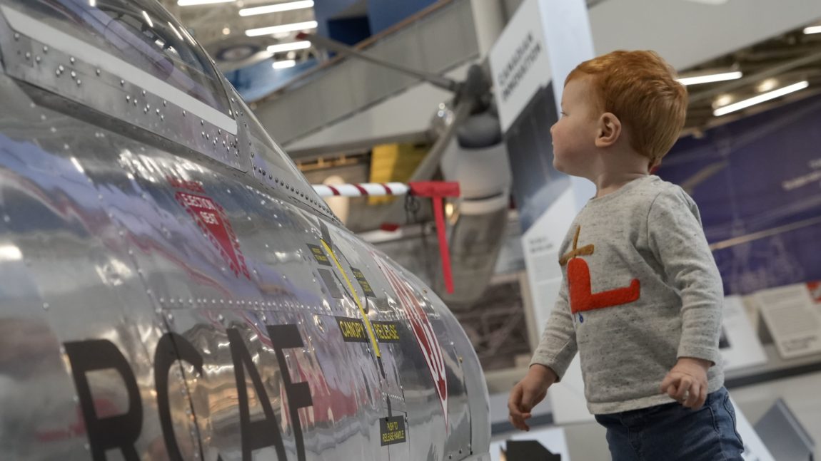 a young boy stares into the cockpit of a fighter jet at an aviation museum