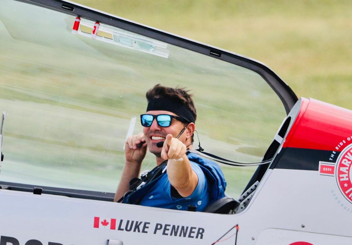 Luke Penner sits in his Extra 300L aerobatic plane. He's wearing blue-tinted aviator sunglasses, looking at the camera and giving a thumbs-up.
