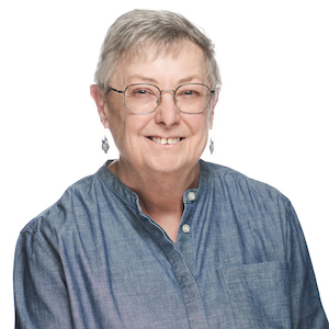 Headshot of a woman with short cropped grey hair wearing glasses and a denim tunic, set against a white backdrop