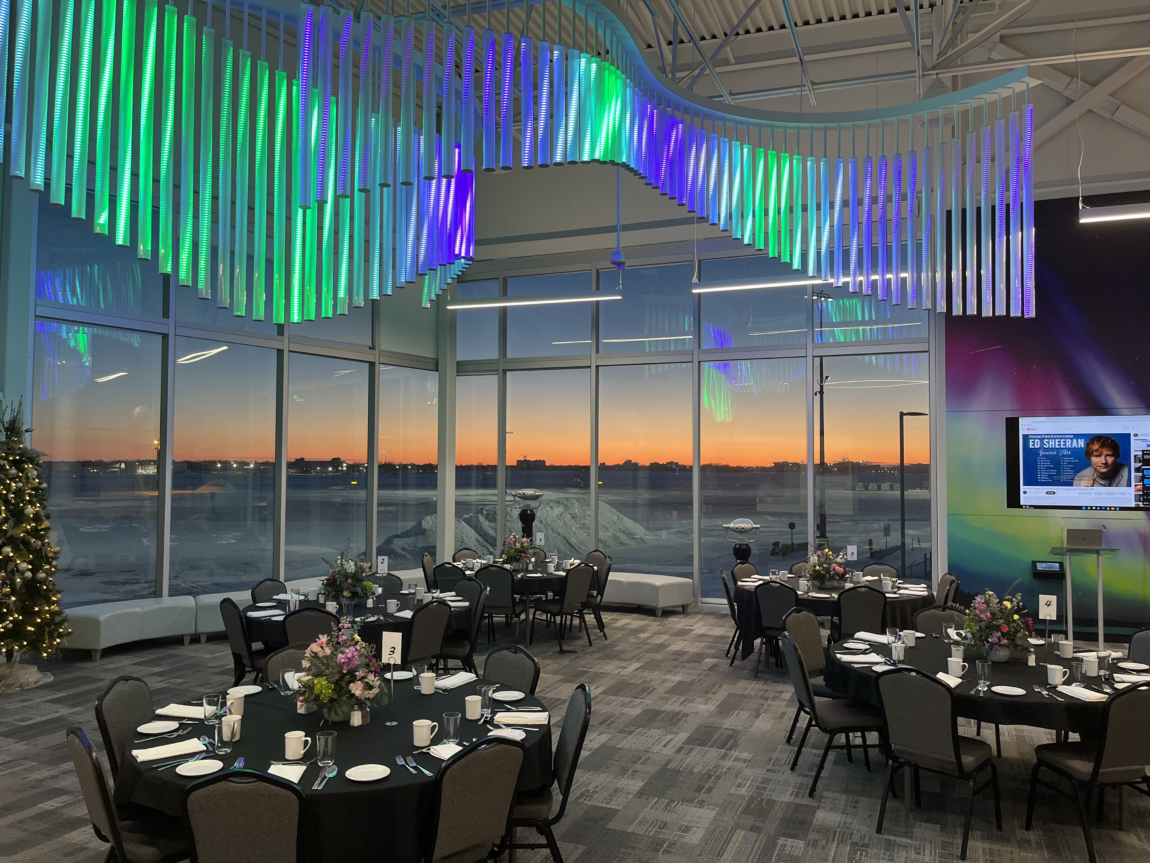 Founders' Observation Lounge at the Royal Aviation Museum. A northern lights art installation hangs above the space, round tables are set for a sit-down dinner. 