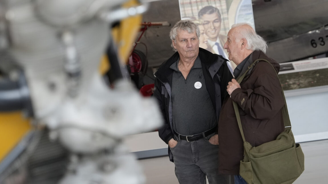 Two gentlemen stand in the galleries discussing aircraft