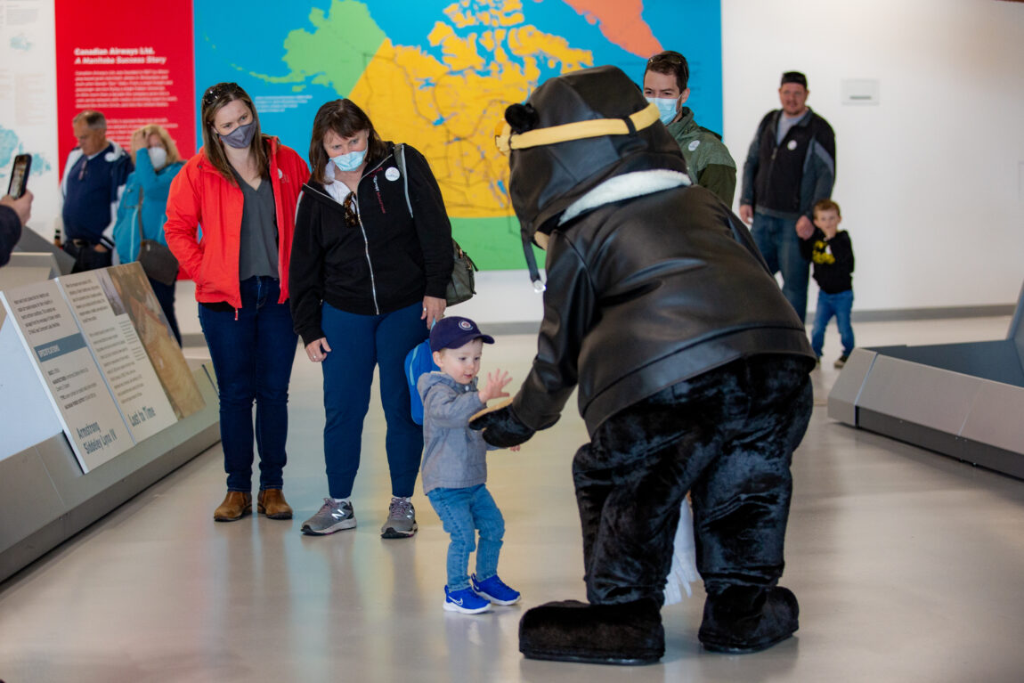 A young visitor gives Hobbs the Bear a high-five at the Royal Aviation Museum