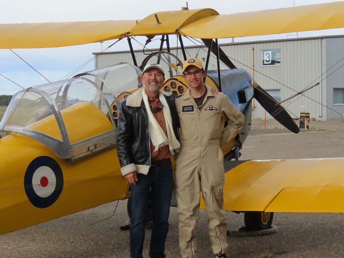 A Commonwealth Air Training Plan Museum visitor and pilot stand next to one of the museum's Tiger Moths after a flight