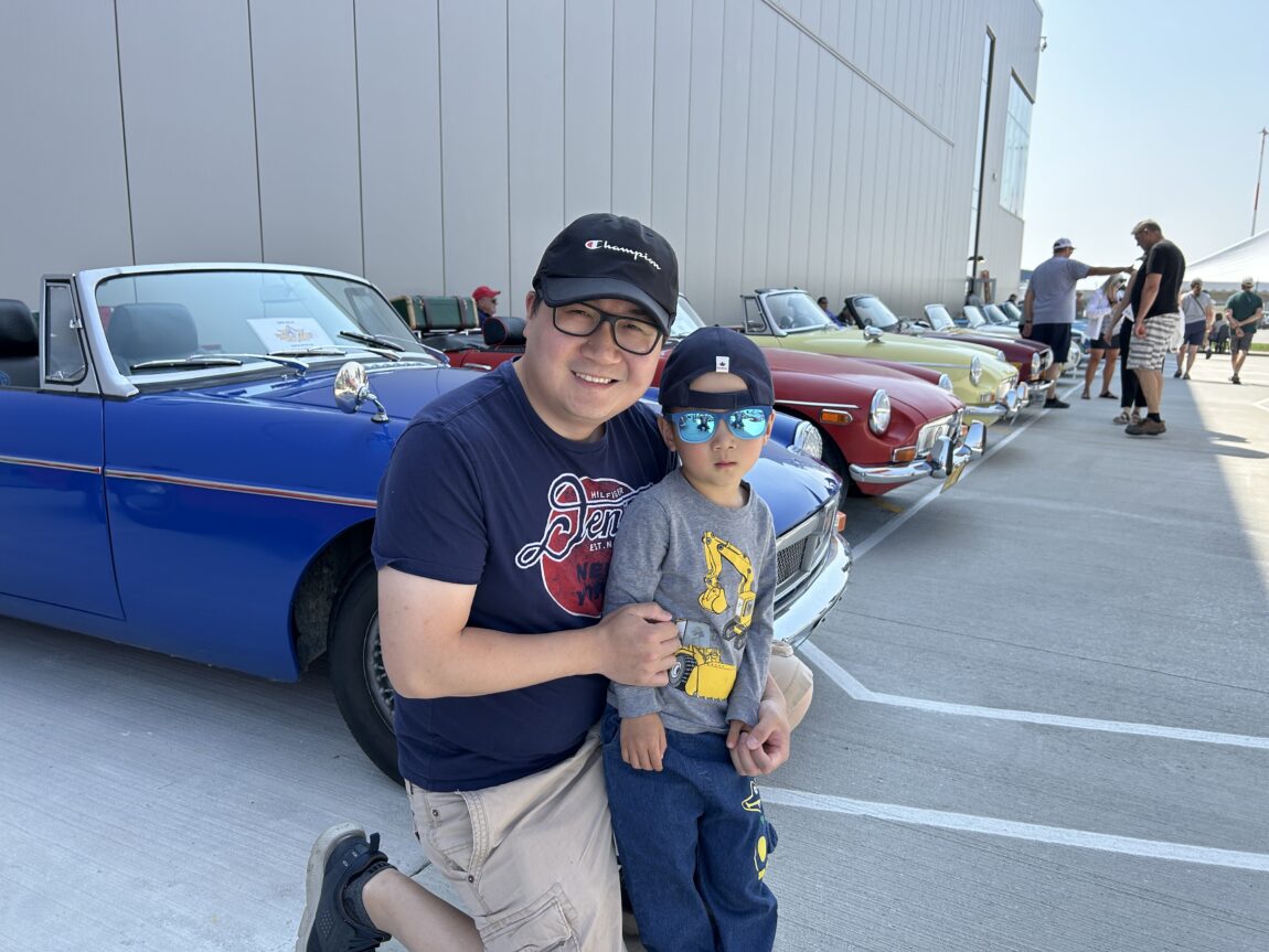 A father and his young son pose crouched down next to a row of classic cars during the Royal Aviation Museum's 'Wings & Wheels' Father's Day event