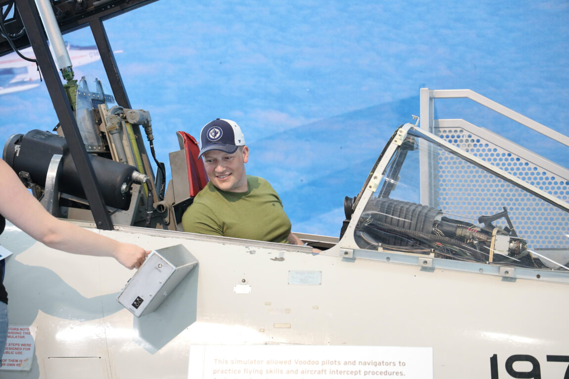 A man sits in the Voodoo trainer at the Royal Aviation Museum. He's looking off to the side and smiling.