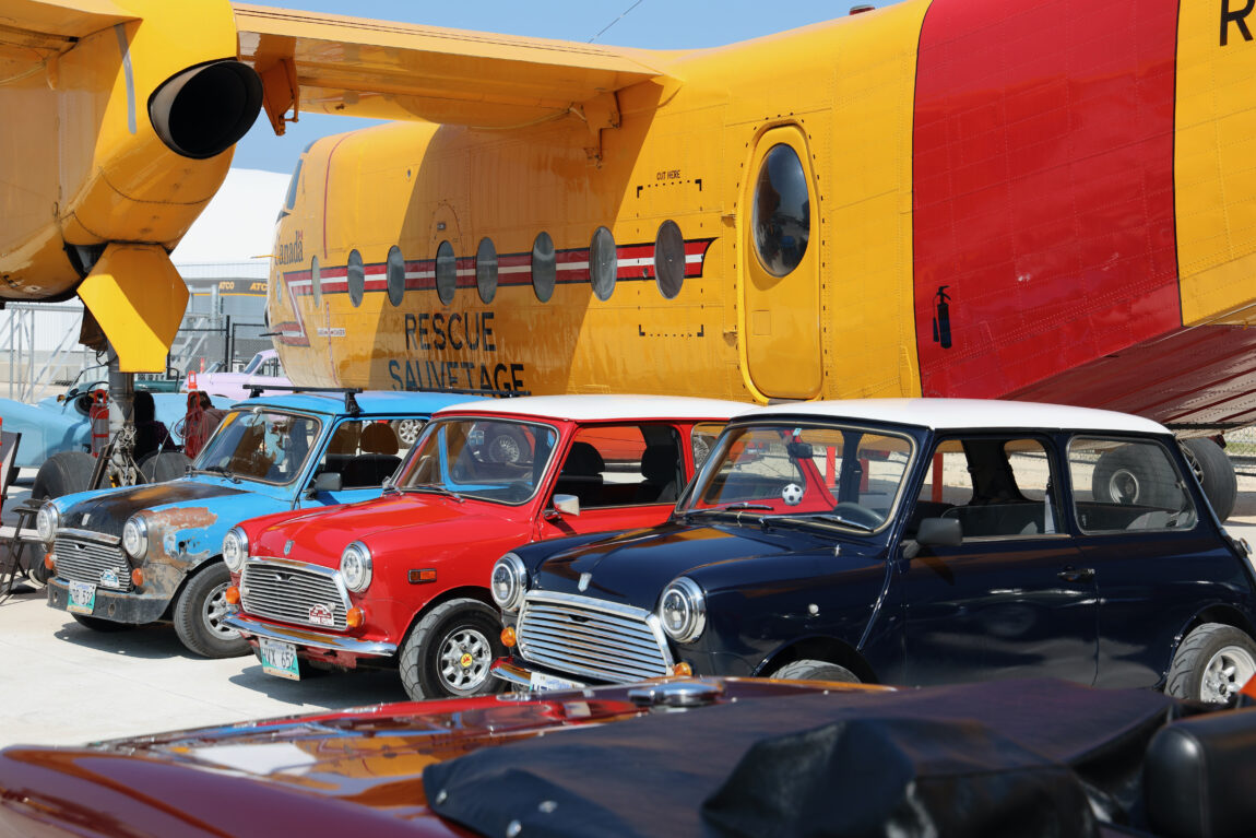A row of Austin Mini cars is parked in front of the CC-115 Buffalo stationed in Aviation Plaza at the Royal Aviation Museum of Western Canada
