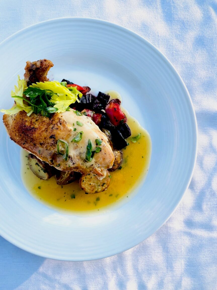 A roasted chicken breast is plated atop a Marsala wine sauce and roasted root vegetables, garnished with slivered green onions and parsley leaves