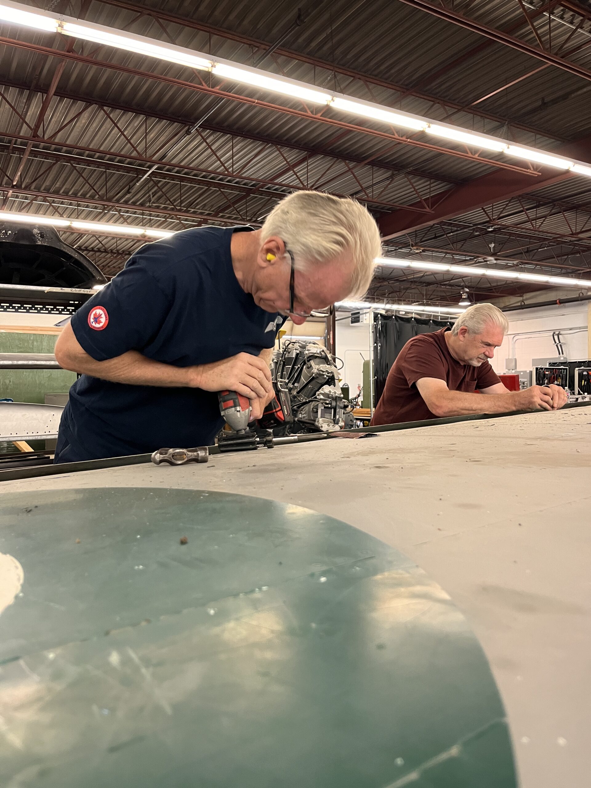 Two men use power tools to disassemble the wing of an aircraft.
