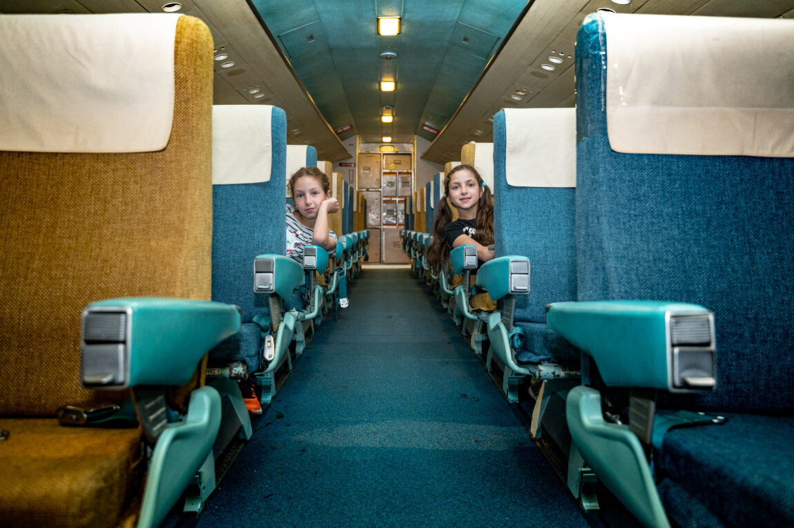 two girls sit across the aisle from each other in a vintage commercial aircraft