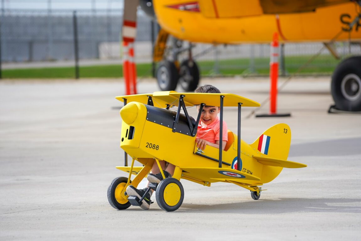 A young child sits in a wooden yellow plane