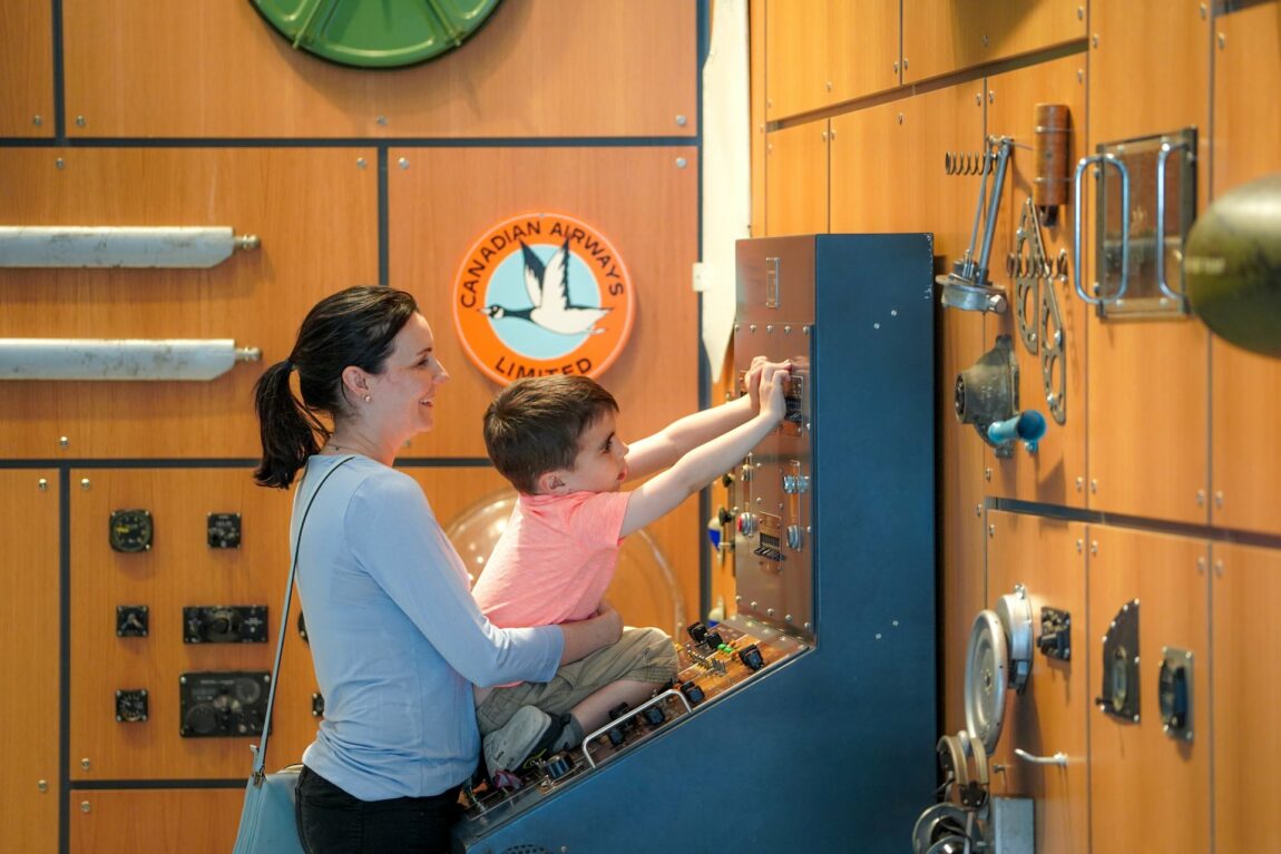 A mother holds her young son up to play with an interactive museum display