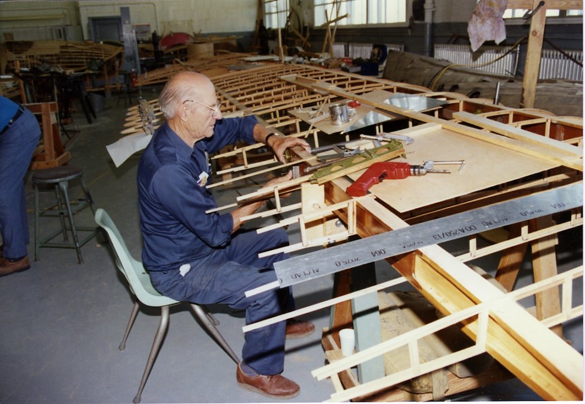 A man sits works on constructing a vintage airplane wing