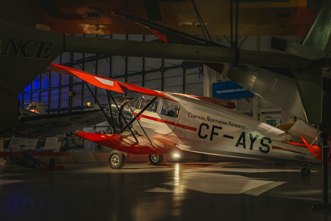 A Waco Sesquiplane in low light at the Royal Aviation Museum, framed by the wings of other aircraft