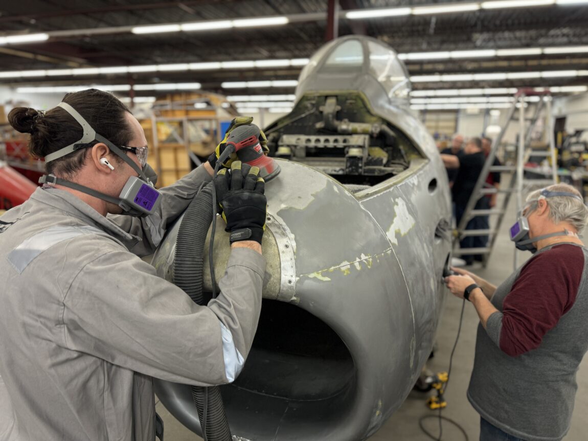An aircraft mechanic sands the nose of a vintage aircraft under restoration