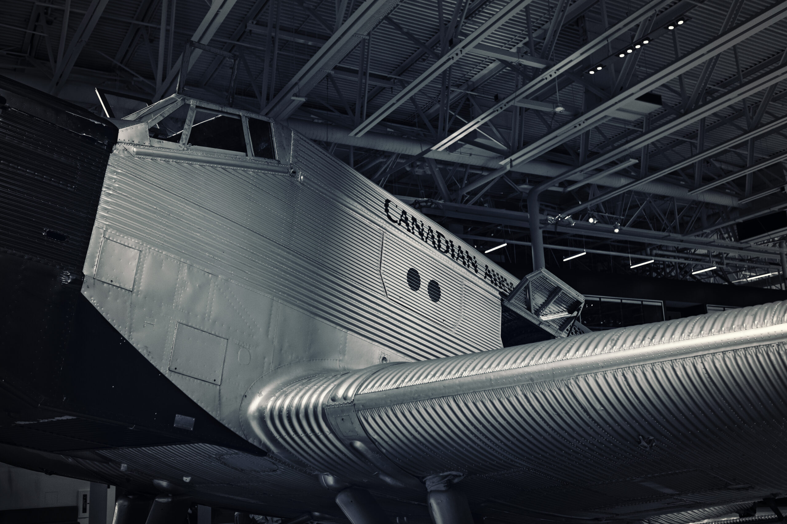 Close-up, black and white image of a large antique cargo plane parked inside a hangar.