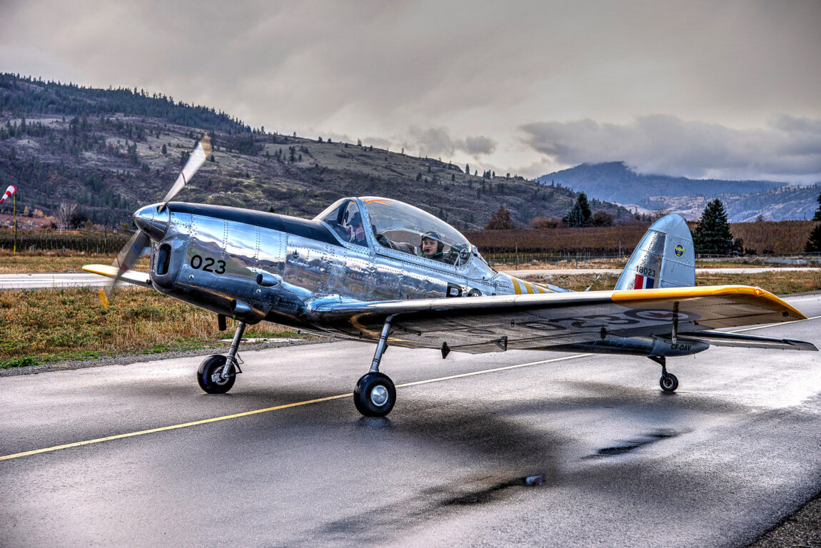 deHavilland Chipmunk aircraft parked on a rainy airstrip. In the background, mountain are visible.