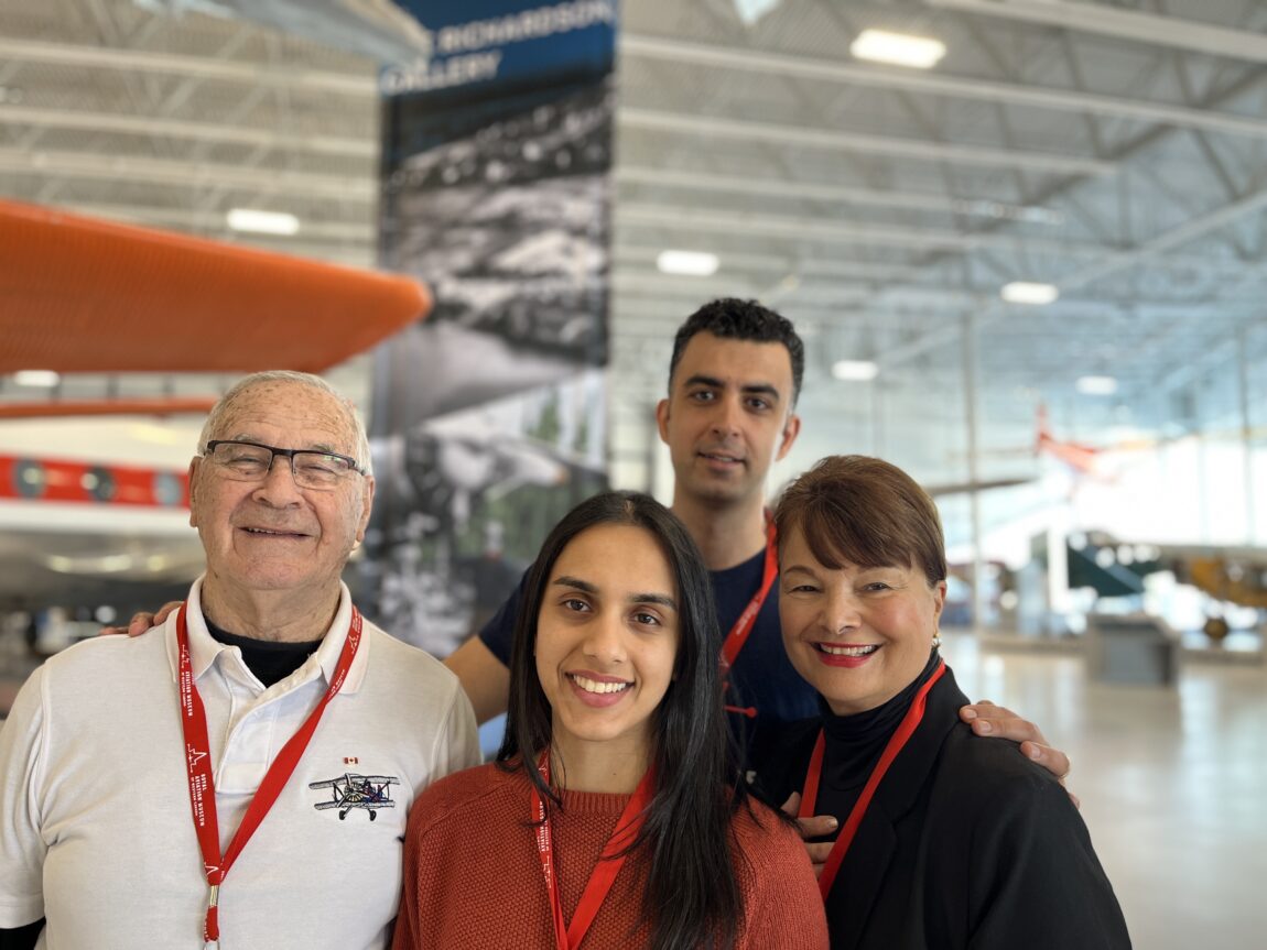 Smiling volunteers stand surrounded by aircraft in an aviation museum