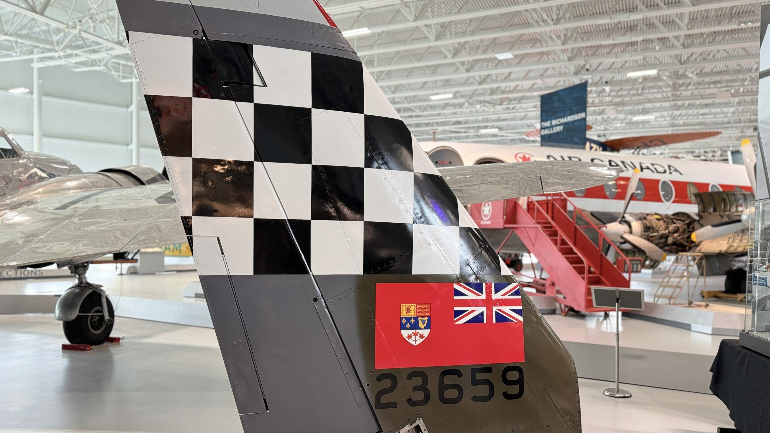 Vertical stabilizer of a vintage F-86 Sabre fighter jet painted with a checkerboard pattern and Manitoba flag on display at the Royal Aviation Museum 